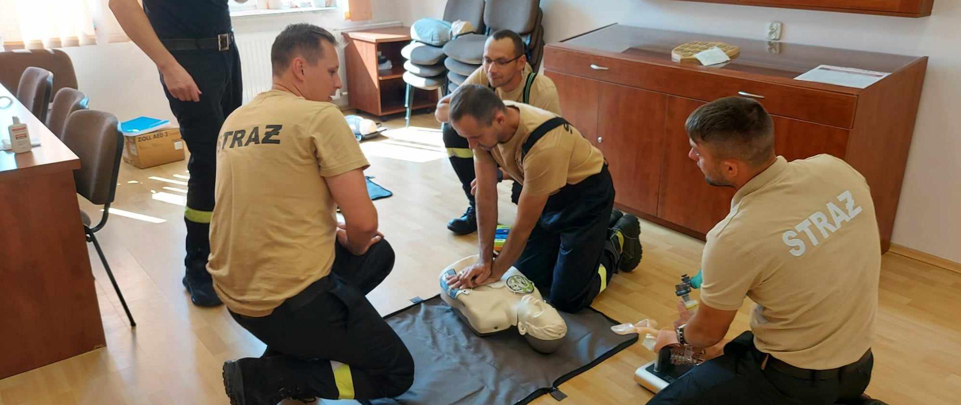 Strażacy druhowie podczas części praktycznej egzaminu z kwalifikowanej pierwszej pomocy. Jeden ze strażaków wykonuje masaż serca na fantomie.