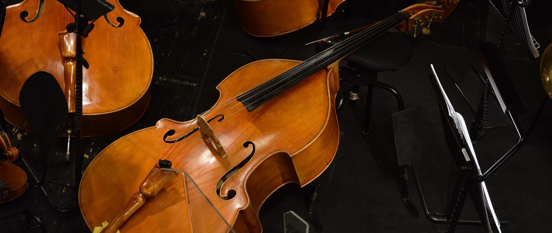 3 kontrabasy oparte o krzesła na scenie leżą pomiędzy pulpitami