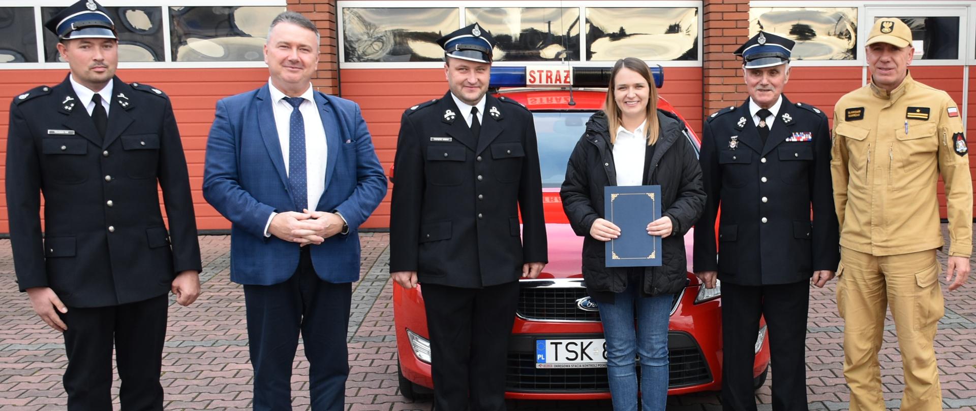 Wspólne zdjęcie Komendanta Powiatowego, samochodu operacyjnego Ford Mondeo druhów OSP i Wójta gminy Skarżysko Kościelne. W tle bramy garażowe JRG Skarżysko-Kamienna