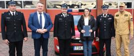 Wspólne zdjęcie Komendanta Powiatowego, samochodu operacyjnego Ford Mondeo druhów OSP i Wójta gminy Skarżysko Kościelne. W tle bramy garażowe JRG Skarżysko-Kamienna