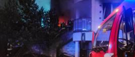 Na zdjęciu widać część budynku przez którego okna wychodzą płomienie oraz rotę strażaków przygotowaną do wejścia do wnętrza palącego się mieszkania 