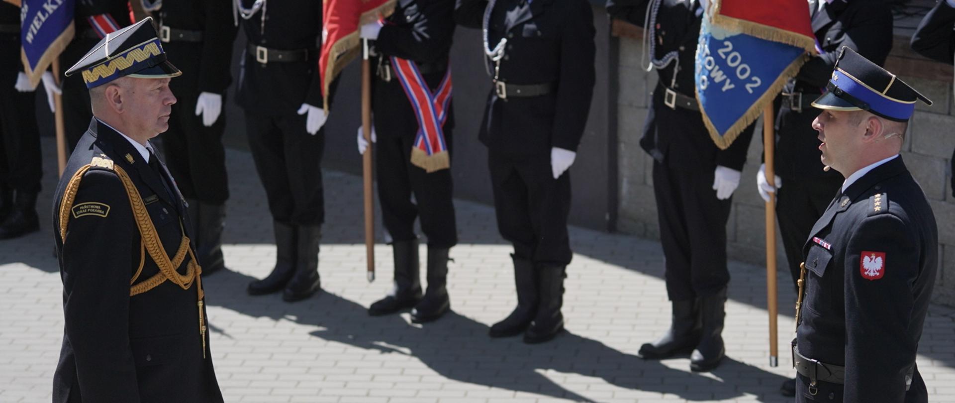 Na zdjęciu widać grupę strażaków. W tle poczty sztandarowe straży pożarnej.