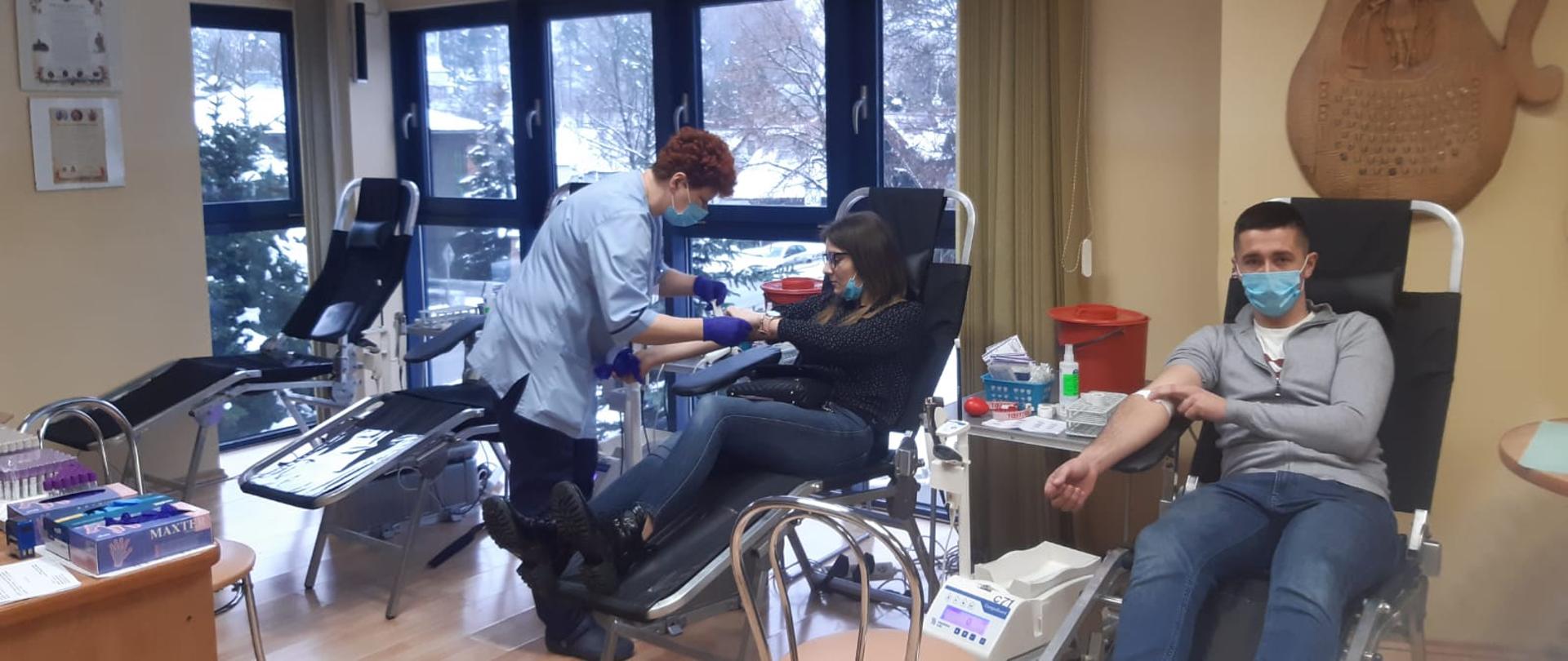 Dwie osoby oddają krew a obok pielęgniarka.