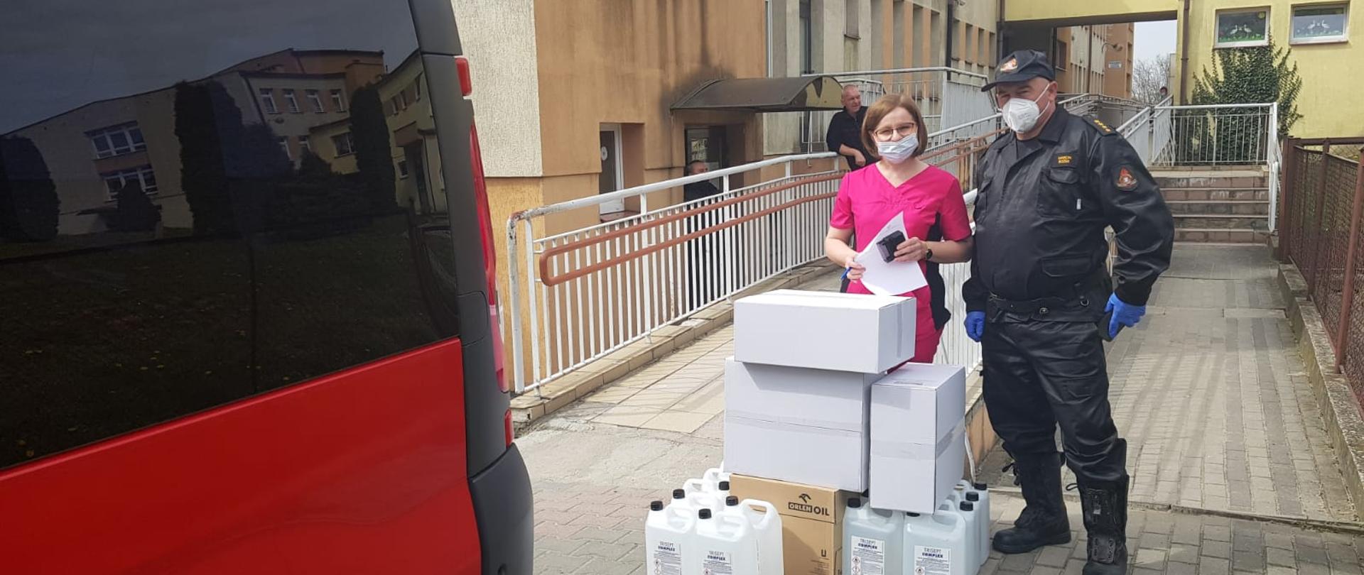 Strażak przekazuje środki ochrony indywidualnej personelowi medycznemu w punkcie sczepień 