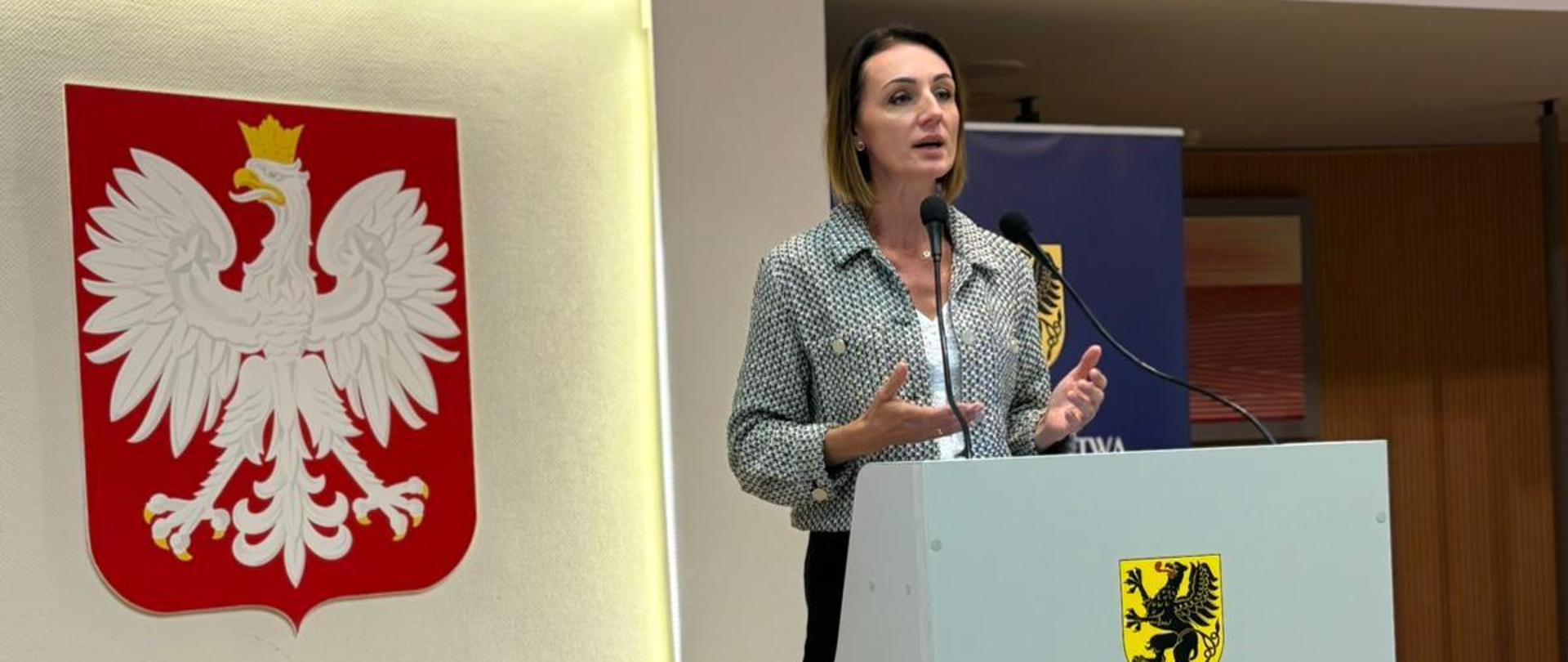 Wojewoda mówi do mikrofonu, w tle godło Polski