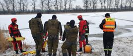 Zdjęcie grupowe ratowników KP PSP Inowrocław i żołnierzy WOT stojących w kierunku zamarzniętego akwenu wodnego. Trwa instruktaż przed przystąpieniem do ćwiczeń praktycznych