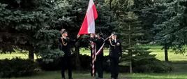 3 strażaków wiesza i wciąga flagę Rzeczypospolitej Polskiej na maszt