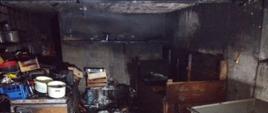 Wnętrze piwnicy budynku mieszkalnego jednorodzinnego po pożarze. Wyposażenie piwnicy częściowo spalone.