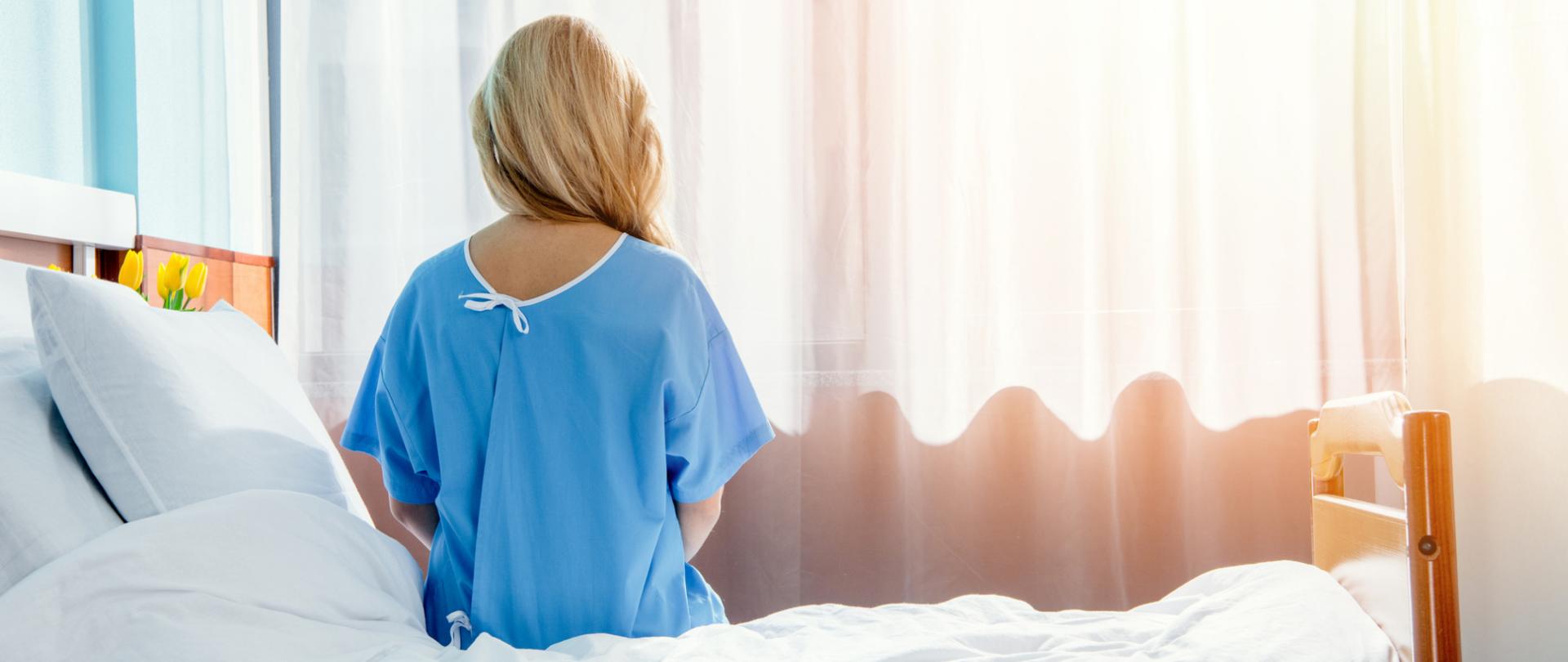 Na zdjęciu jest kobieta siedząca na łóżku. Postać jest widziana z tyłu.