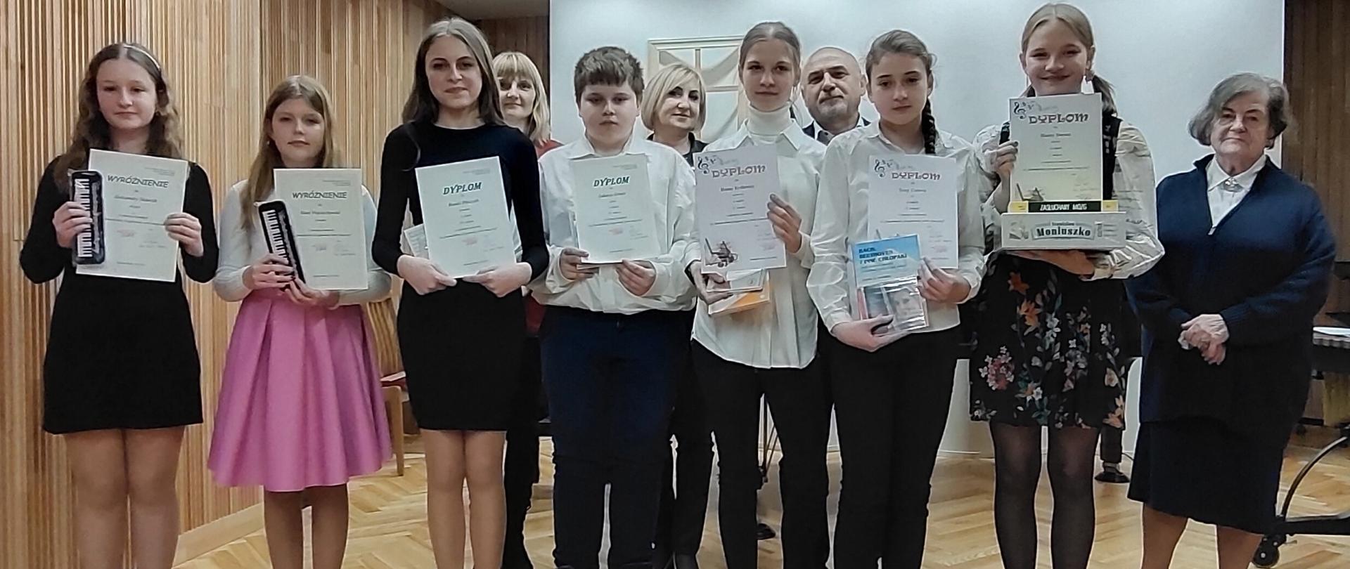 Zdjęcie przedstawia stojących na scenie laureatów Szkolnego konkursu na samodzielne przygotowanie utworu w roku szkolnym 2023/2024 wraz z jurorami