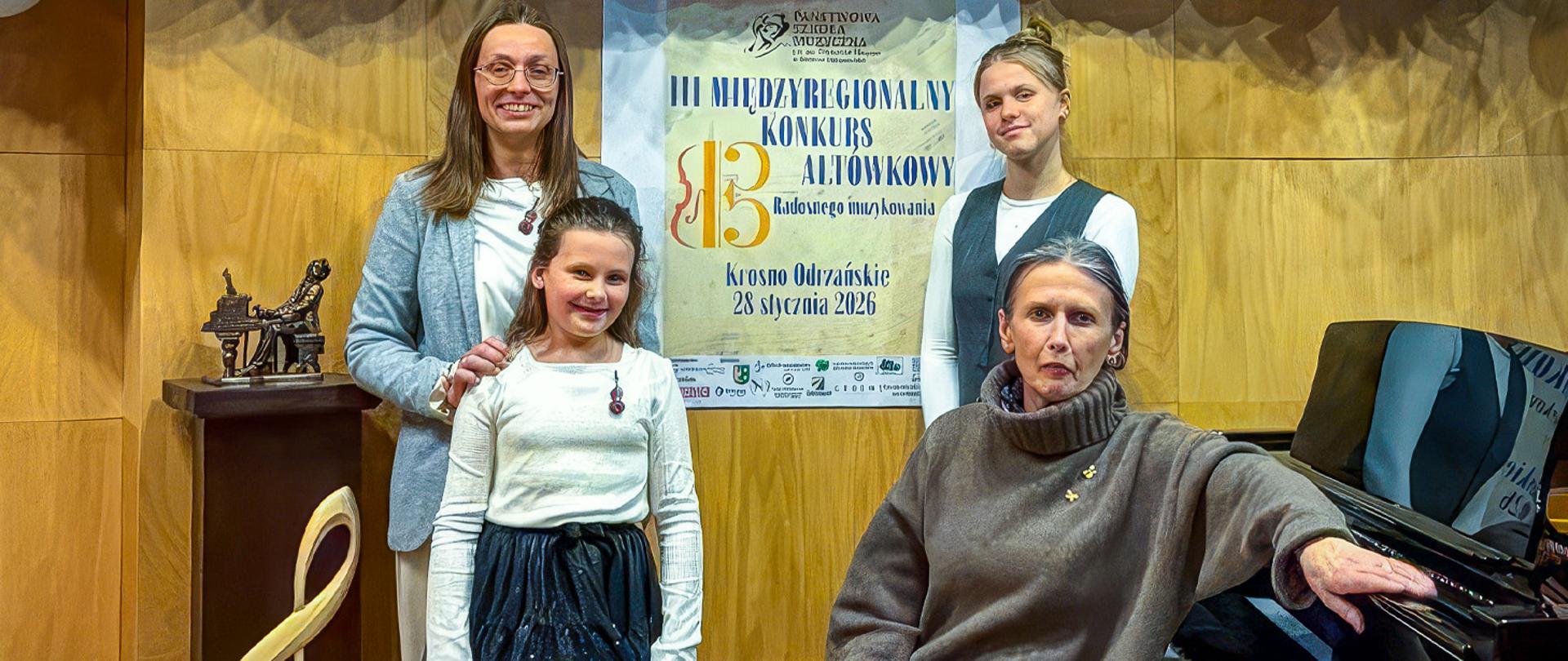 Dwie nauczycielki i dwie uczennice stoją obok fortepianu na tle plakatu promującego konkurs altówkowy.