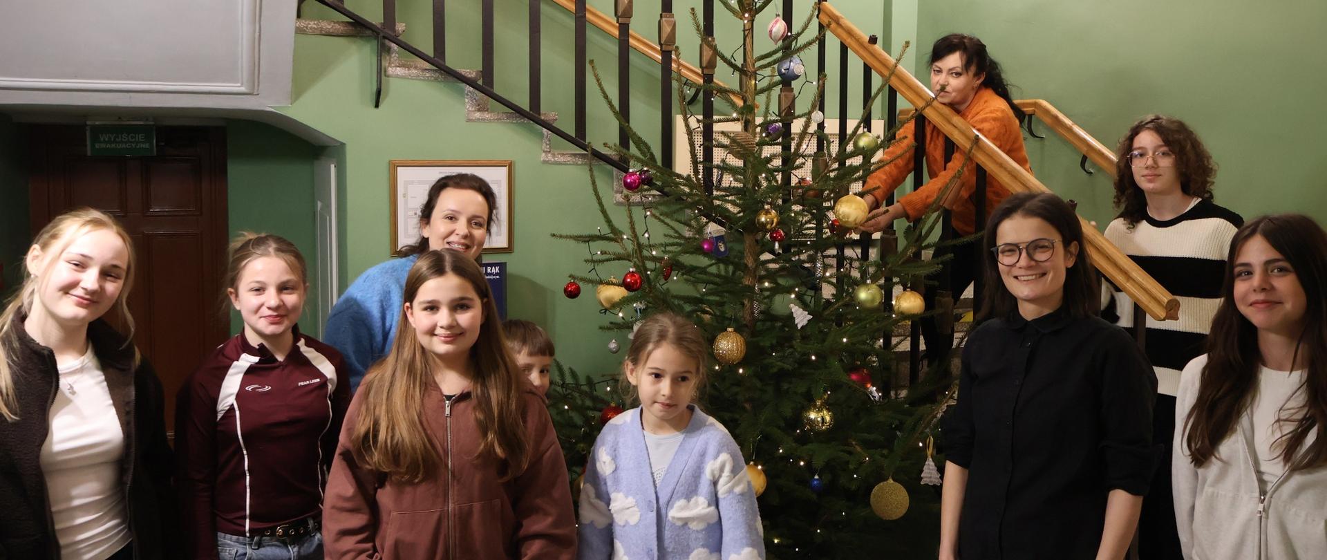 Grupa osób w holu szkoły przy ubranej choince.