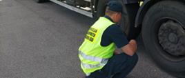 Umundurowany inspektor warmińsko-mazurskiej ITD kontroluje stan bieżnika opon na kołach naczepy ciężarowej.