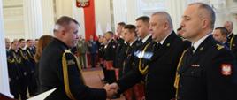 Na zdjęciu widzimy oficerów Państwowej Straży Pożarnej stojących na baczność odbierających awanse na wyższe stopnie.