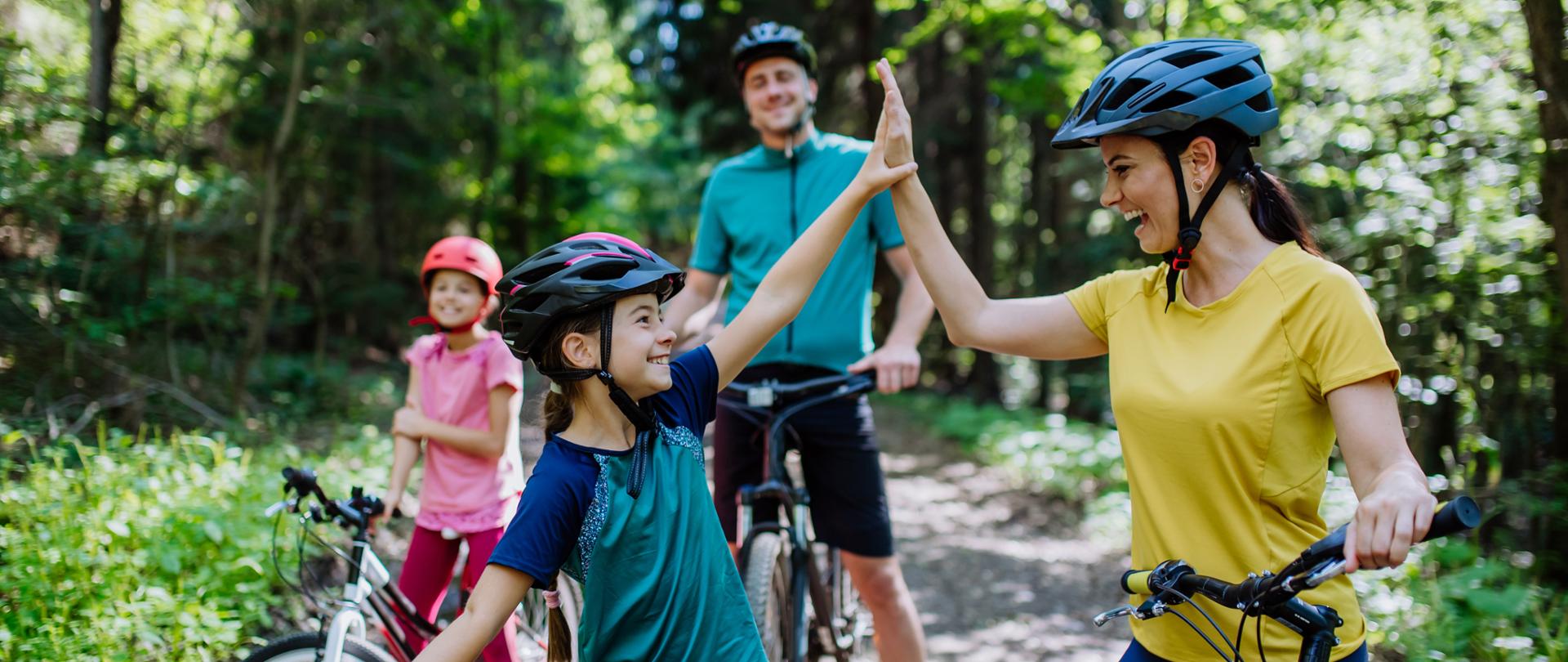 A young family with little children preapring for bike ride, standing with bicycles in nature and high fiving.