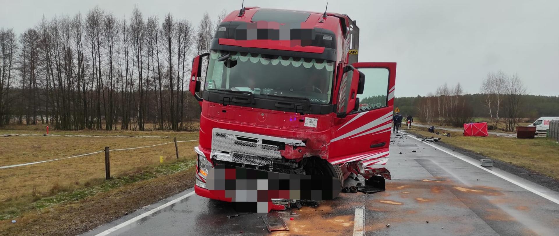 Zdjęcie przedstawia stojący na drodze pojazd ciężarowy z rozbitym przodem, z którego wylały się płyny eksploatacyjne