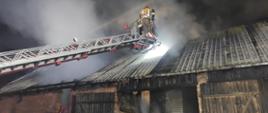 Pożar budynku gospodarczego, przed budynkiem strażacy w koszu drabiny strażackiej.