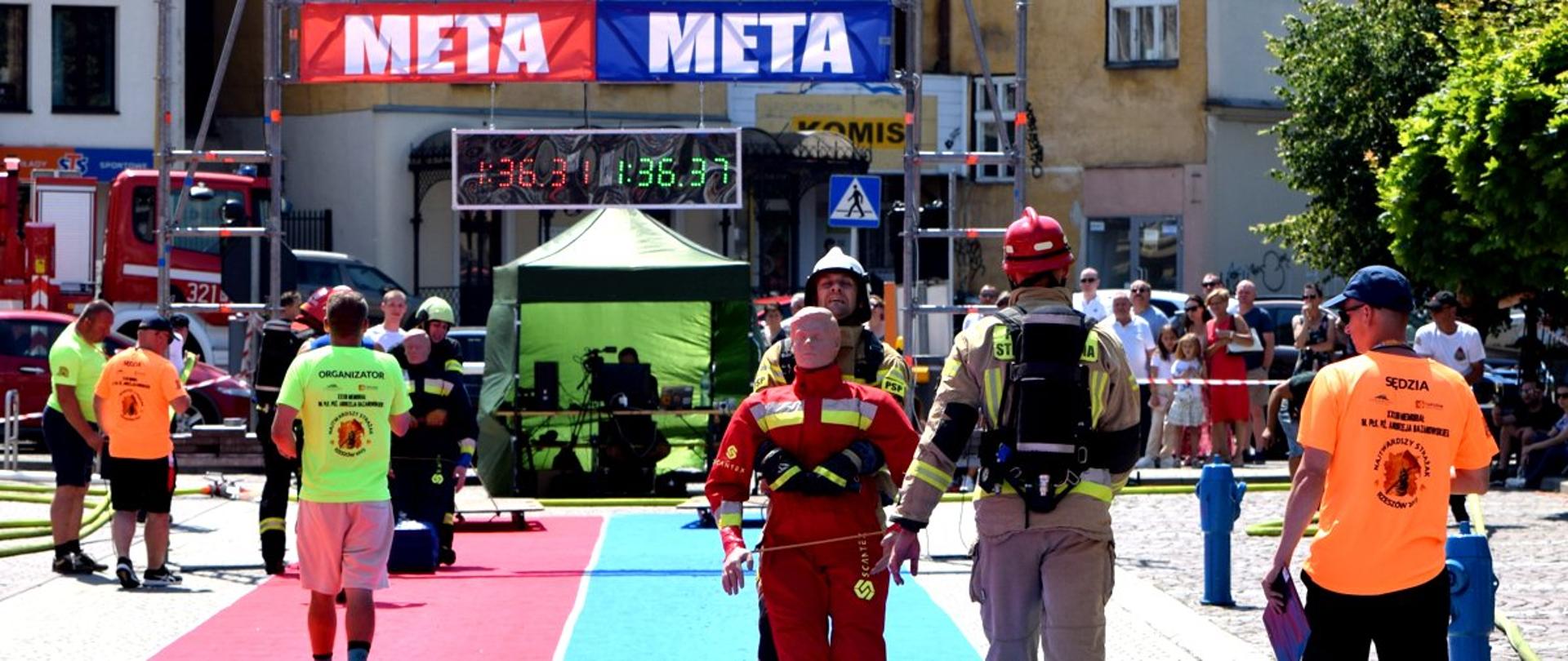 Zdjęcie zrobione na zewnątrz, na placu przy Podkarpackim Urzędzie Wojewódzkim w Rzeszowie podczas rozgrywania zawodów strażackich. Strażacy startują w konkurencji.