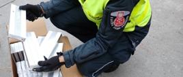 Funkcjonariusz Służby Celno-Skarbowej przy kartonie z papierosami.