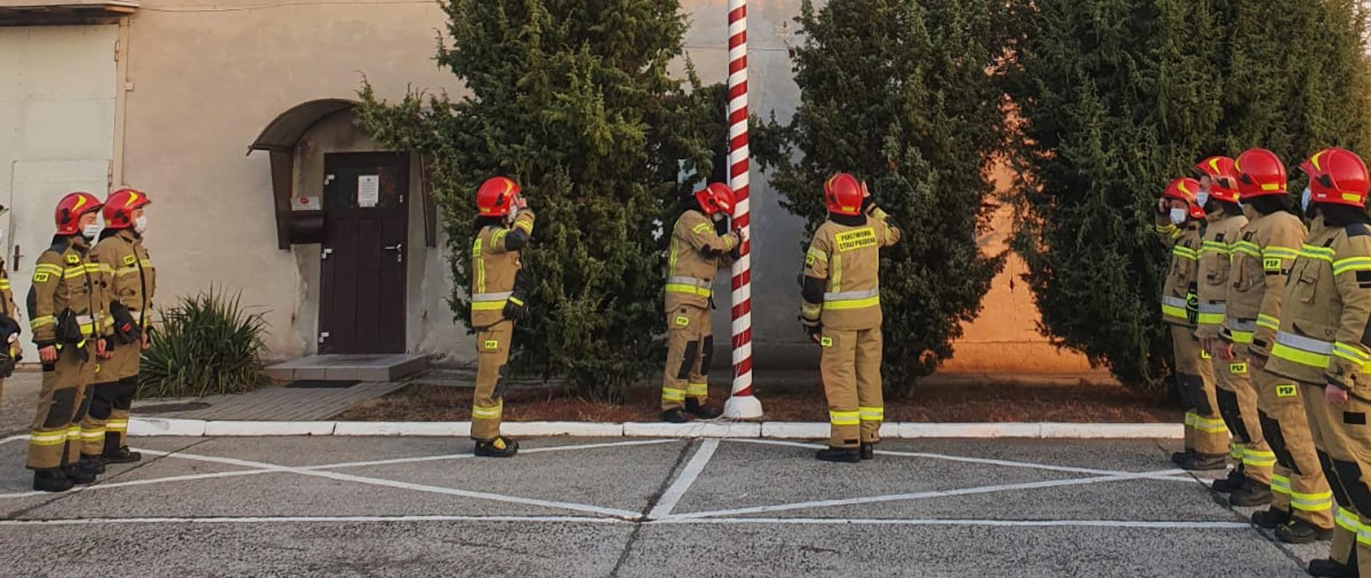Na placu komendy powiatowej państwowej straży pożarnej w Żarach podczas zmiany służbowej strażacy z dwóch zmian uroczyście przekazują służbę z okazji 103 rocznicy odzyskania niepodległości przez Polskę. Jest wciągana flaga na maszt i odegrany hymn Polski. 