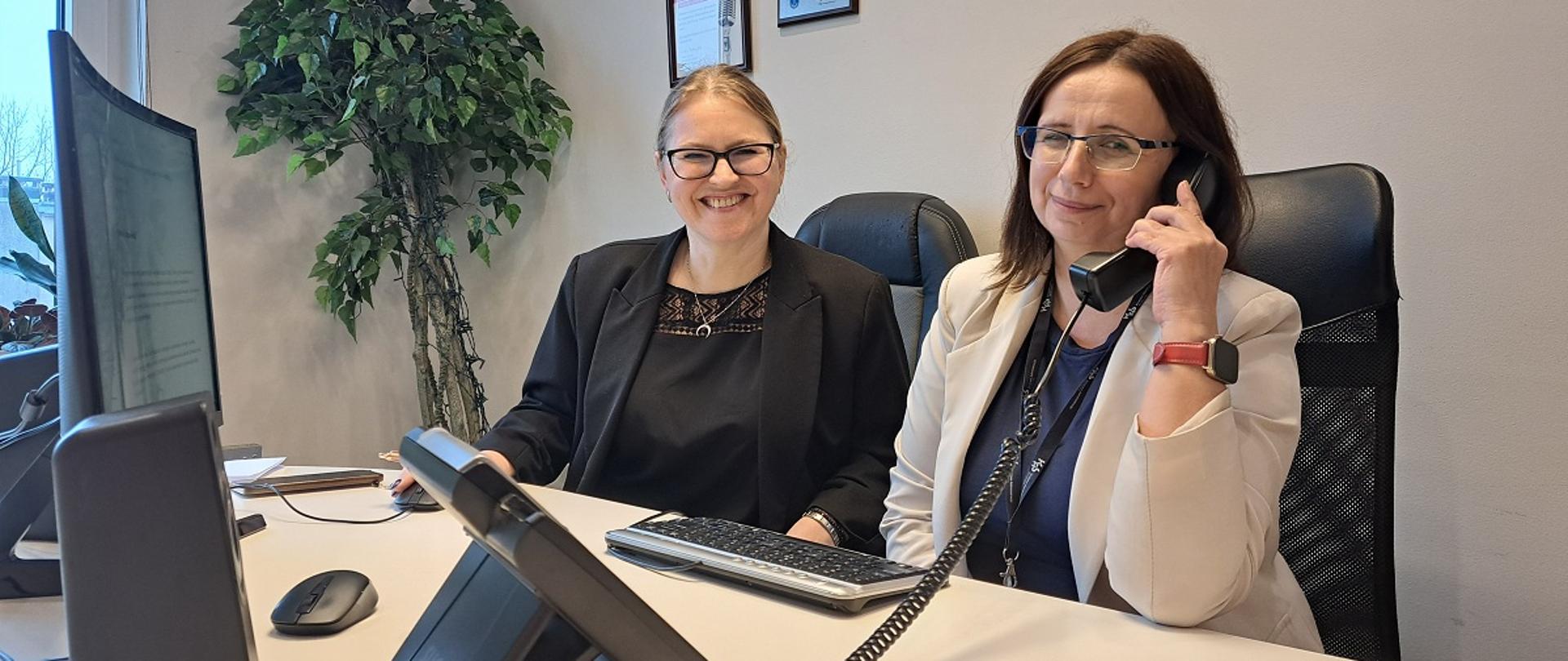 Pracownice urzędu siedzą przy biurku. Jedna z nich rozmawia przez telefon