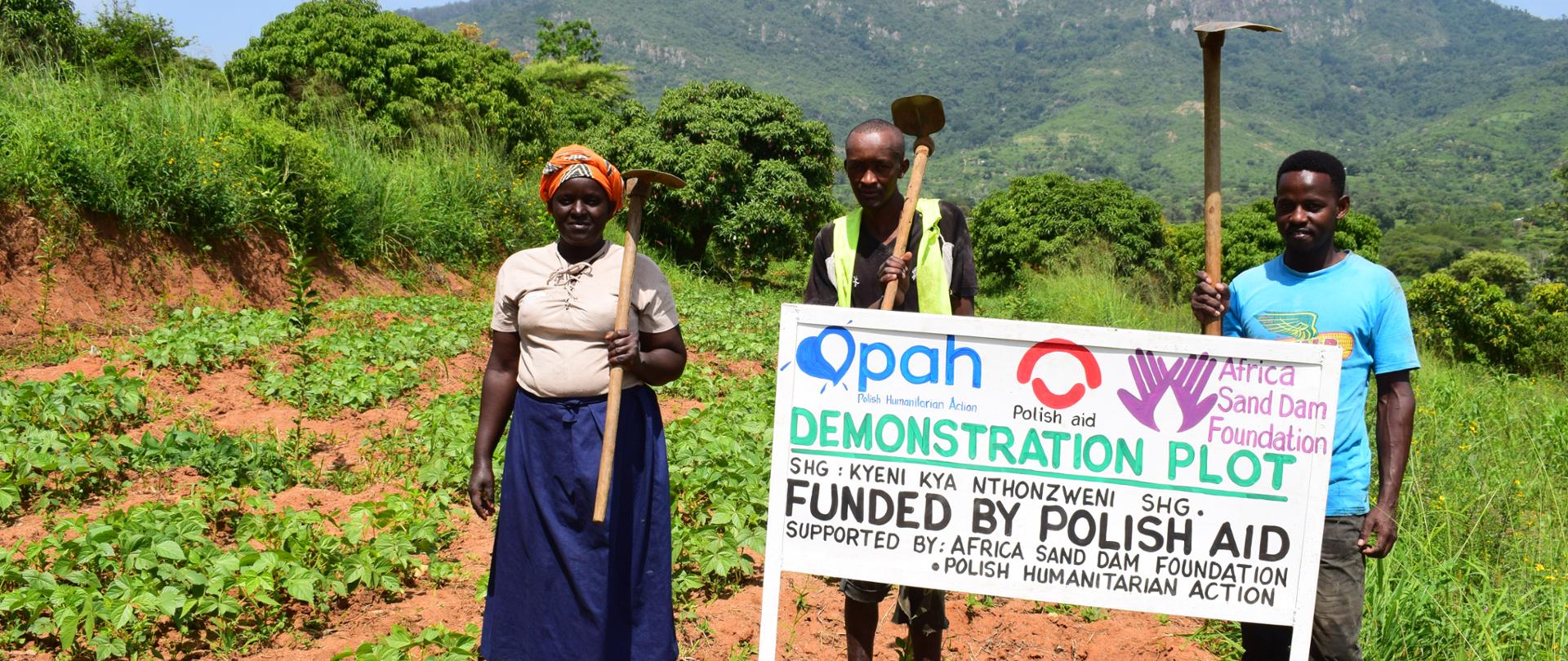 Dwóch mężczyzn i kobieta na modelowym polu uprawnym z tablicą informacyjną