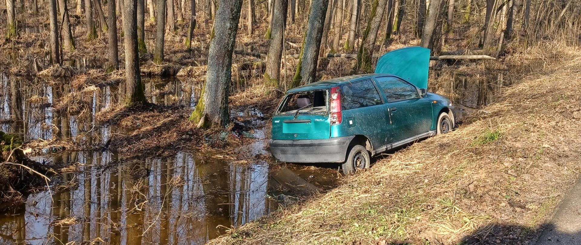 Samochód osobowy znajduje się w przydrożnym rowie. Ma podniesioną maskę oraz wybita tylna szybę. 