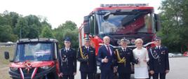 Funkcjonariusze Państwowej Straży Pożarnej, druhowie ochotniczej straży pożarnej oraz zaproszeni gości stoją przed pojazdami ratowniczymi.