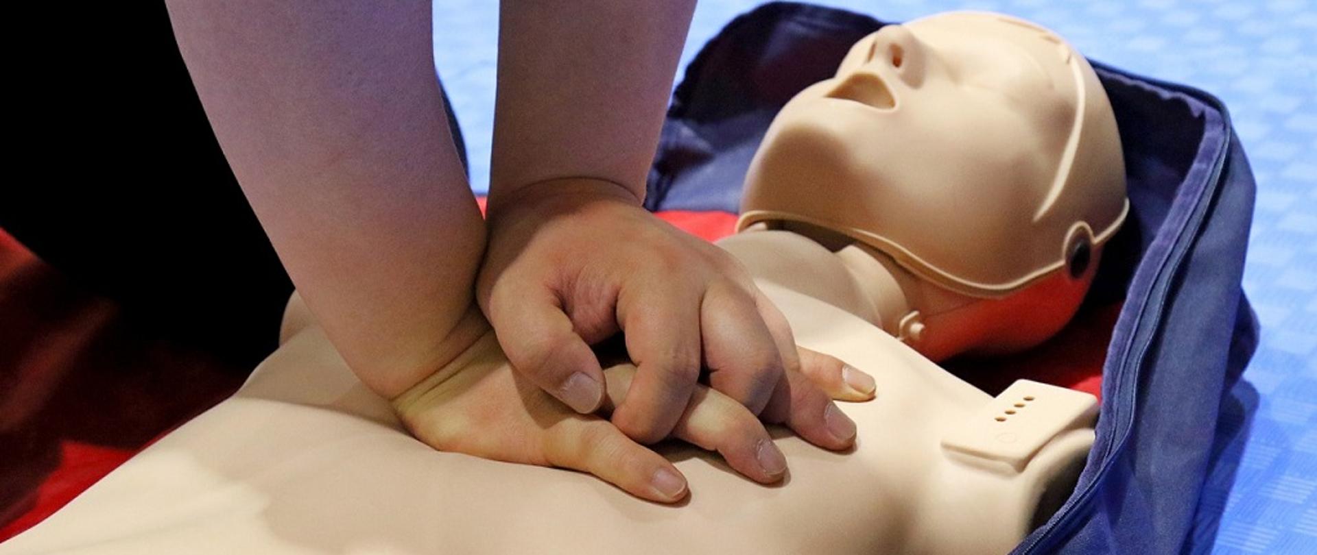 fantom, leżący na ziemi, na którym ktoś ćwiczy zasady resuscytacji