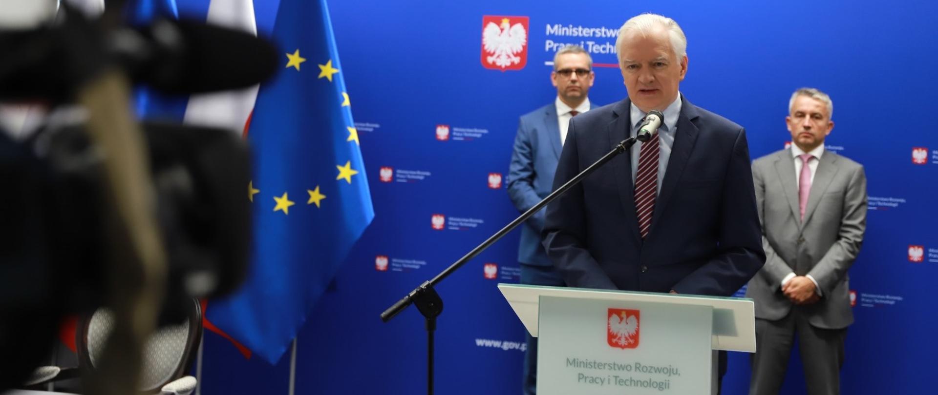 Wicepremier Jarosław Gowin stoi przed mównicą i mówi do kamery. Z tyłu stoją prezes PAIiH Krzysztof Drynda i honorowy prezydent ABSL Jacek Levernes.