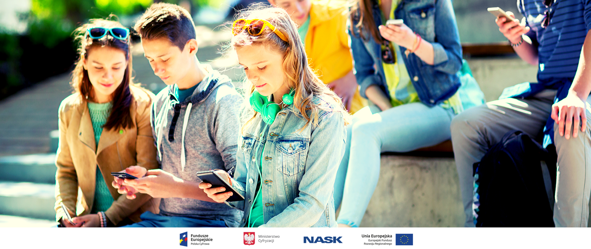 Kilkoro nastolatków siedzi na schodach, trzymają telefony i wpatrują się w ich ekrany