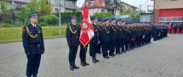 Kompania strażaków złożona z PSP I OSP stoją na placu wraz sztandarami na obchodach dnia strażaka. 