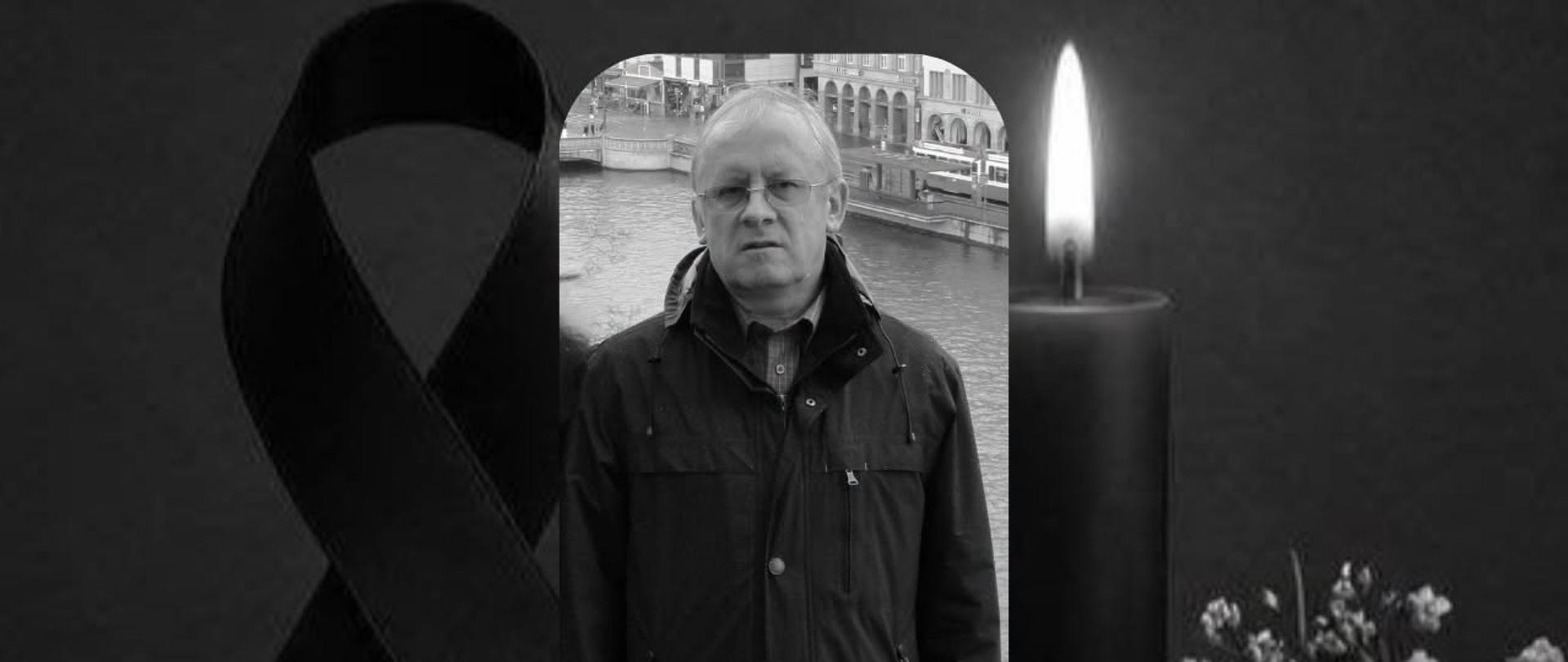 Czarno-biała grafika żałobna. Po lewej znajduje się czarna wstążka, po prawej zapalona świeca i białe kwiaty. Pośrodku umieszczono fotografię Dariusza Ratajczaka.