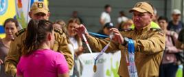 Zdjęcie przedstawia biegacza podczas biegu 14 Przemyska Dycha, zastępca dowódcy jednostki ratowniczo gaśniczej w Przemyślu wręcza medal, obok zastępca komendanta miejskiego PSP