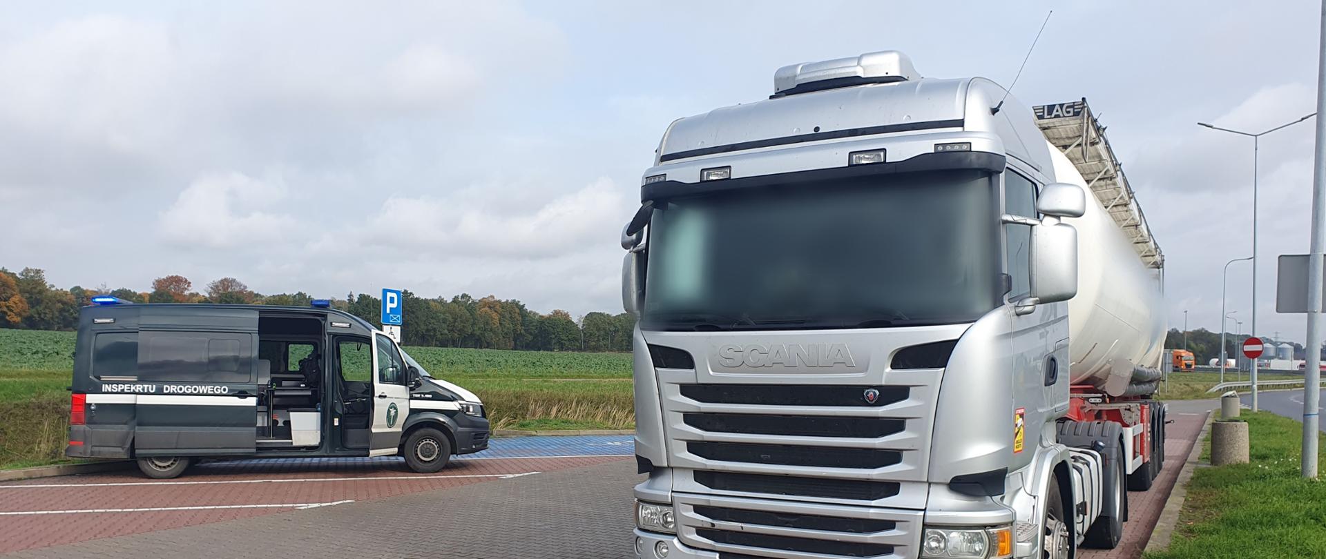 "Srebrny ciągnik siodłowy Scania z naczepą-cysterną, sfotografowany z przodu, zaparkowany na parkingu. W tle, po lewej stronie, widoczny jest furgon Inspekcji Transportu Drogowego (ITD) z otwartymi drzwiami i niebieskimi sygnałami świetlnymi."