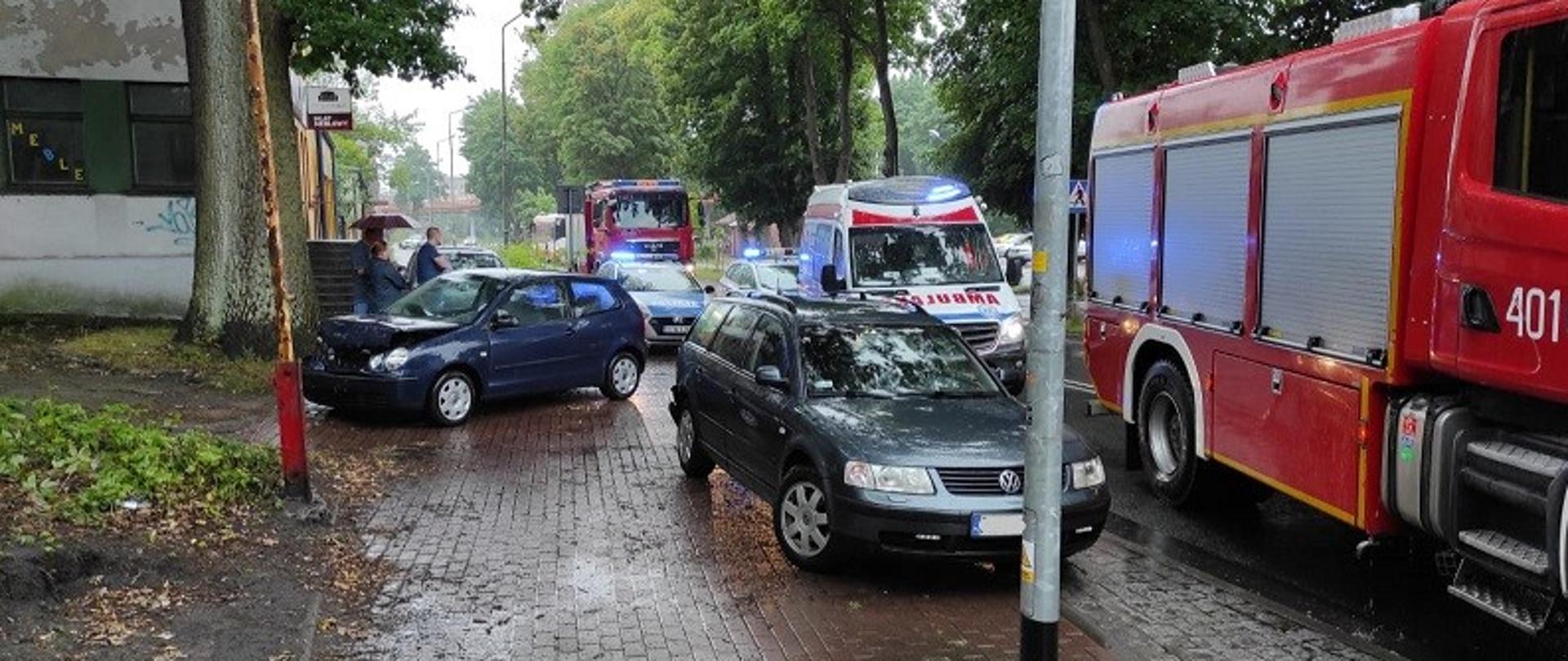 Zdjęcie przedstawia ulicę Drzymały w Białogardzie, gdzie doszło do kolizji pojazdów. Na zdjęciu stojące na chodniku pojazdy VW Polo i VW Passat. Na ulicy stoją pojazdy straży pożarnej, pogotowia ratunkowego i policji