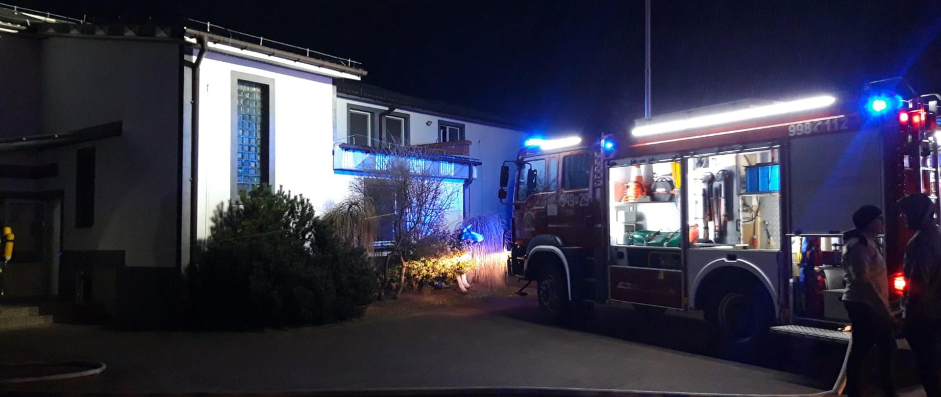 Zdjęcie przedstawia działania jednostek ochrony przeciwpożarowej podczas akcji gaśniczej pożaru budynku ubojni bydła. Na zdjęciu widać pojazd ratowniczo - gaśniczy podczas działań oraz budynek w którym wybuchł pożar. Zdjęcie wykonane w porze wieczornej na terenie zakładu ubojni bydła.