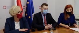 Sekretarz Stanu w MEN Marzena Machałek, Minister Edukacji i Nauki Przemysław Czarnek i Rzecznik Prasowy MEN Anna Ostrowska siedzą przy stole. W tle flaga Polski i Unii Europejskiej.