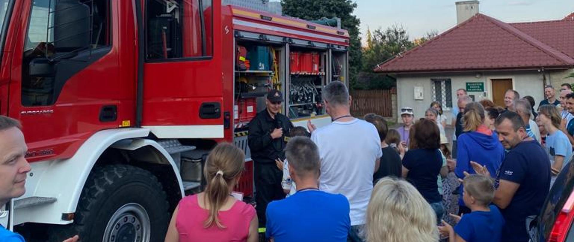 Zdjęcie przedstawia rodziny oglądające sprzęt strażacki będący na wyposażeniu samochodu ratowniczo-gaśniczego.