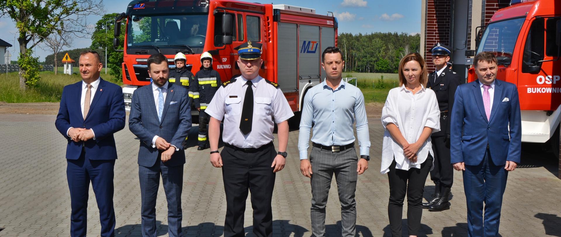 Zdjęcie przedstawia uroczystość poświęcenia wozu bojowego w Bukownicy. Na zdjęciu obecni druhowie OSP Bukownica oraz zaproszeni goście. Zdjęcie wykonane w porze dziennej podczas wręczenia pamiątkowych podziękowań osobom zaproszonym na placu OSP Bukownica.