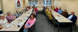 Uczestnicy spotkania z okazji Dnia Kobiet w Komendzie Powiatowej PSP w Obornikach siedzą przy wspólnych stołach podczas poczęstunku. Wśród gości znajdują się funkcjonariuszki, pracownice oraz emerytowane funkcjonariuszki, a także strażacy i zaproszeni goście. Na stołach widoczna jest kawa, herbata i ciasta.