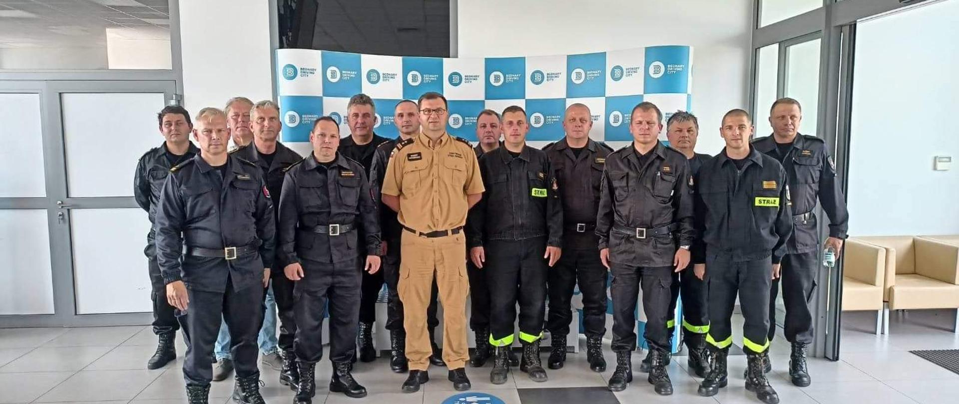 Na zdjęciu widać grupę funkcjonariuszy w umundurowaniu. Zdjęcie pozowane. Wykonane w ciągu dnia. Światło naturalne. Na podłożu szare płytki. Korytarz.