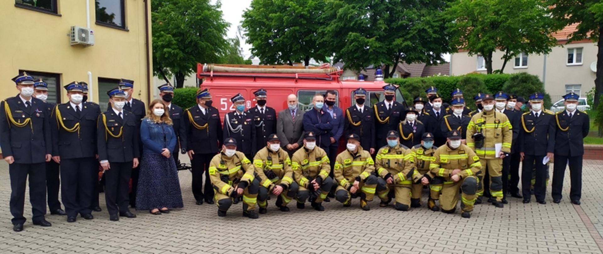 na zdjęciu widać strażaków oławskiej Komendy oraz zaproszonych gości podczas uroczystego apelu z okazji Dnia Strażaka. Zdjęcie pamiątkowe na tle zabytkowego strażackiego Żuka.