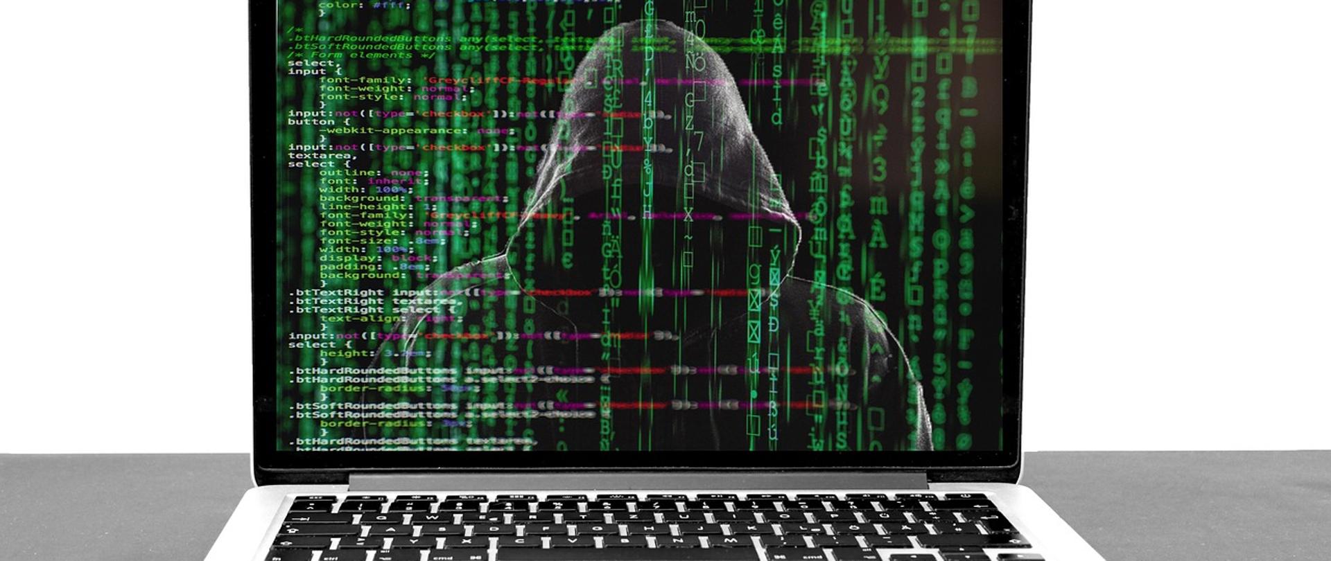 Zakapturzona postać na ekranie laptopa. Na pierwszym planie znaczniki algorytmów i kody