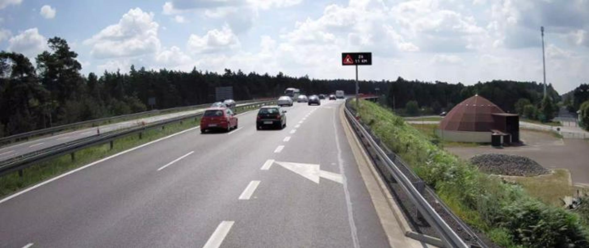 Samochody jadące dwupasową drogą ekspresową. Na zdjęciu widoczny pas włączenia. Po prawej stronie widoczny magazyn do przechowywania soli drogowej.