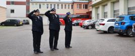 Trzech funkcjonariuszy Państwowej Straży Pożarnej oddaje honor.