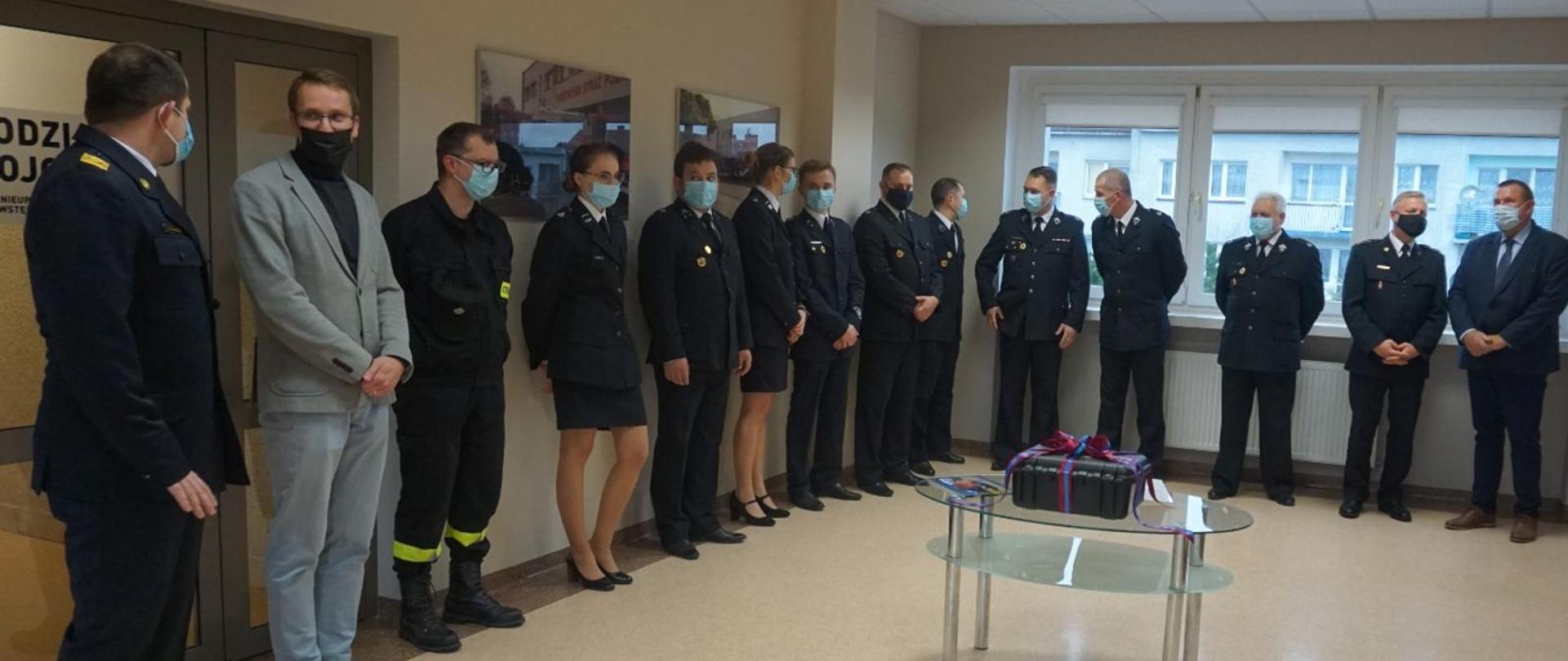 Zbiórka strażaków w pomieszczeniu, na środku dron.