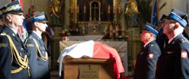 Na zdjęciu uczestnicy mszy pogrzebowej podczas nabożeństwa. Przy trumnie wystawiona jest warta honorowa strażaków oraz poczty sztandarowe.
