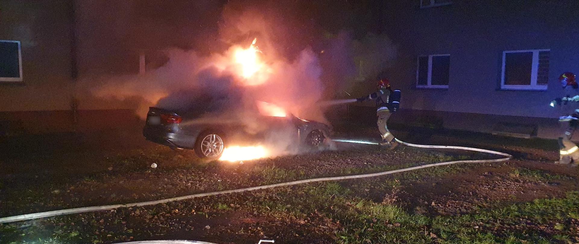 Strażak gasi palący się samochód osobowy poprzez podanie jednego prądu wody.