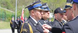 Na zdjęciu widoczni Małopolski Komendant Wojewódzki PSP wręczający strażakom odznaczenia resortowe. Komendant w galowym granatowym mundurze i w czapce rogatywce. Strażacy odbierający odznaczenia ubrani w galowe granatowe mundury i w czapkach rogatywkach.